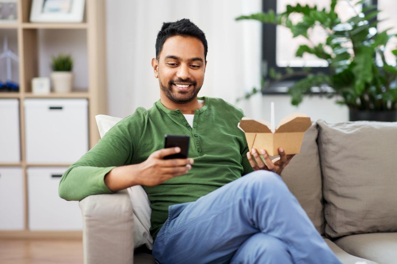 smiling indian man eating takeaway food at home