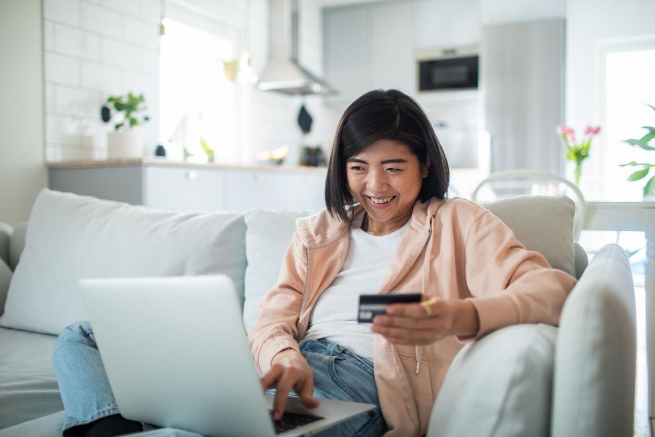 Young woman online shopping on her laptop from the comfort of her couch